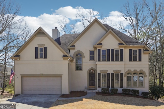 view of front facade with stucco siding, roof with shingles, concrete driveway, an attached garage, and a chimney