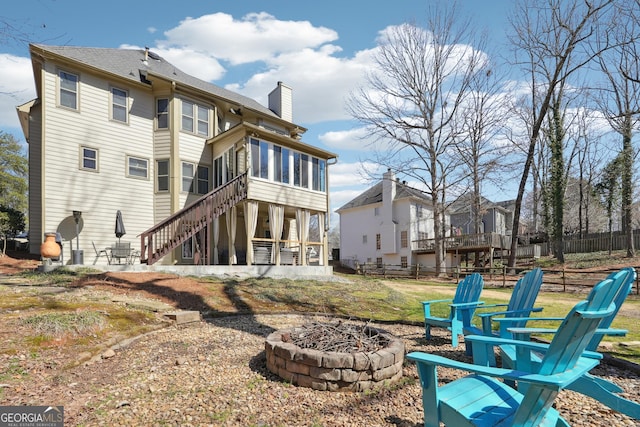 rear view of property with stairway, fence, an outdoor fire pit, a sunroom, and a chimney