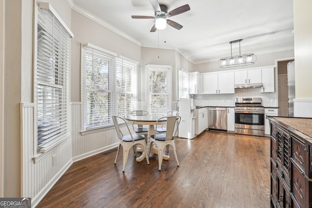 kitchen with dark wood-type flooring, white cabinets, under cabinet range hood, appliances with stainless steel finishes, and crown molding