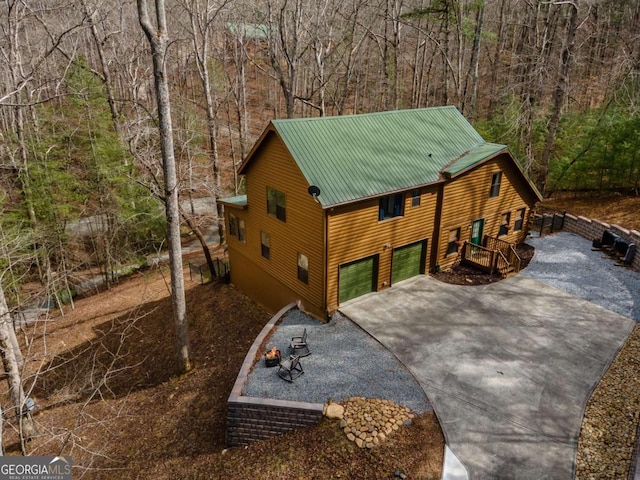 view of front of home with a garage, a wooded view, driveway, and metal roof