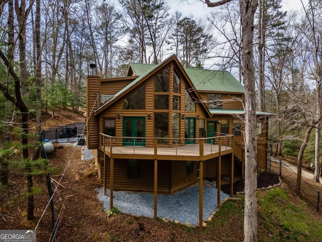 rear view of property with metal roof, a chimney, a wooden deck, and faux log siding