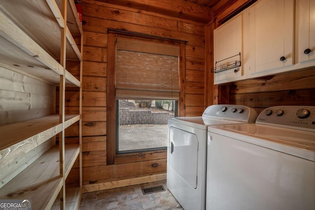 laundry room with visible vents, stone finish floor, washer and dryer, cabinet space, and wood walls