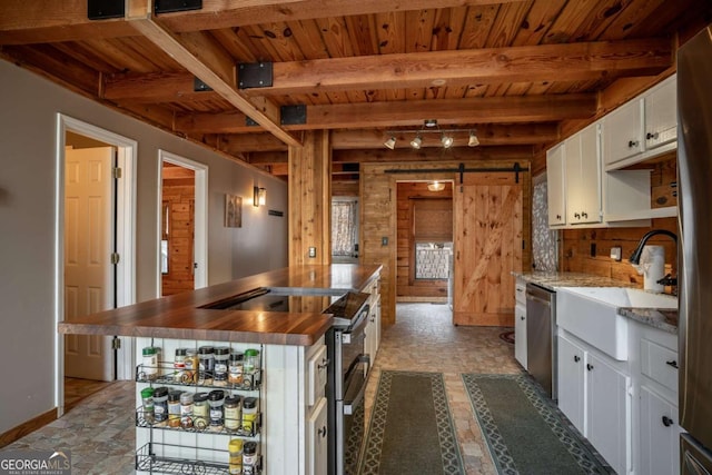 kitchen with a sink, stainless steel appliances, white cabinets, a barn door, and beamed ceiling