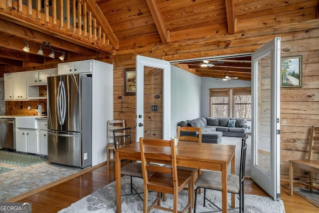 dining room featuring light wood finished floors, lofted ceiling with beams, french doors, wood walls, and wooden ceiling