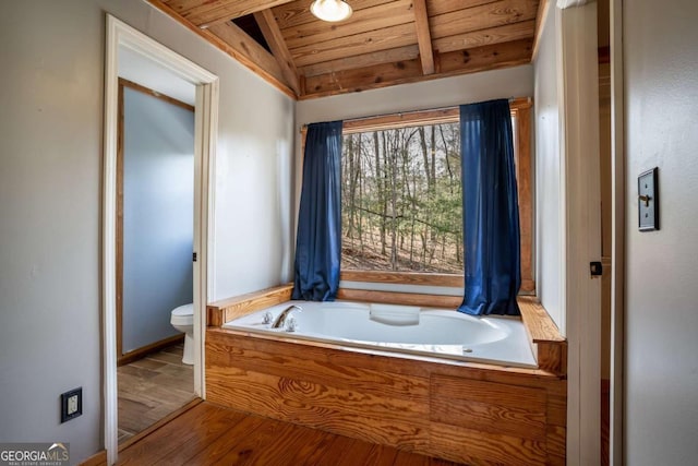 bathroom with toilet, lofted ceiling with beams, wood finished floors, wood ceiling, and a bath