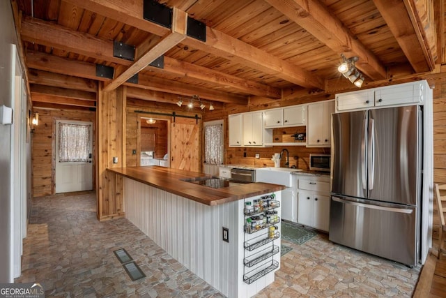 kitchen featuring butcher block countertops, a barn door, appliances with stainless steel finishes, and wood walls