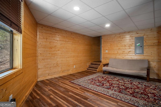 unfurnished room with electric panel, a paneled ceiling, wooden walls, and wood finished floors