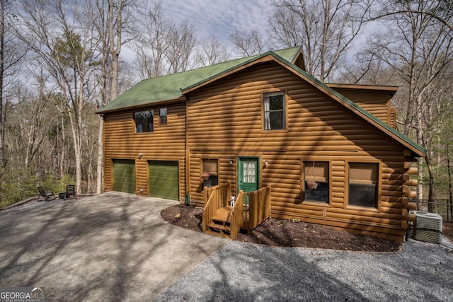 log cabin featuring central air condition unit, an attached garage, and driveway