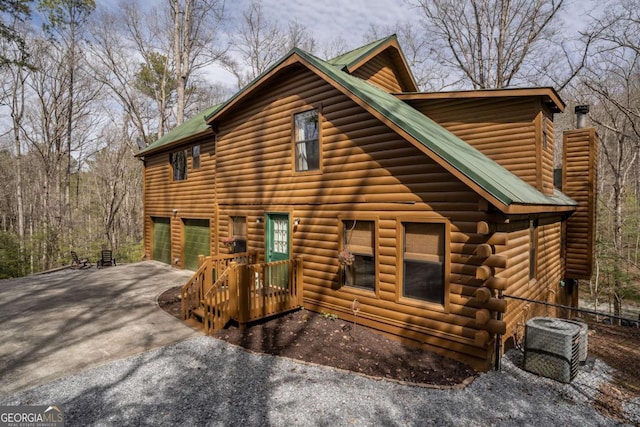 log cabin with an attached garage, cooling unit, driveway, and metal roof