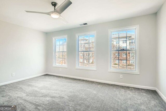 carpeted spare room with a wealth of natural light, visible vents, baseboards, and a ceiling fan
