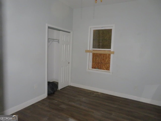 unfurnished bedroom with dark wood-style floors, baseboards, and a closet