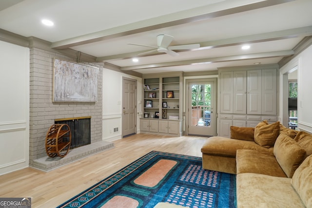 living area with beam ceiling, light wood finished floors, ceiling fan, and a brick fireplace