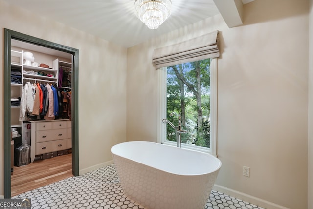 full bathroom featuring a walk in closet, baseboards, a freestanding bath, and an inviting chandelier