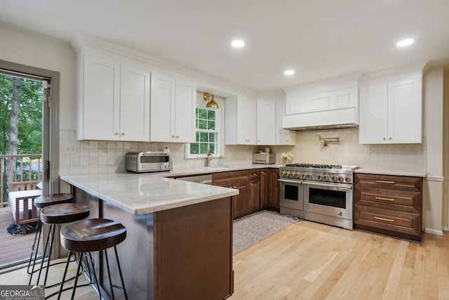 kitchen featuring light wood-type flooring, a kitchen bar, custom range hood, white cabinetry, and stainless steel appliances