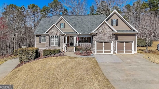 craftsman-style home with an attached garage, covered porch, concrete driveway, a front lawn, and stone siding