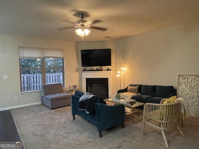 living area with a glass covered fireplace, baseboards, and ceiling fan