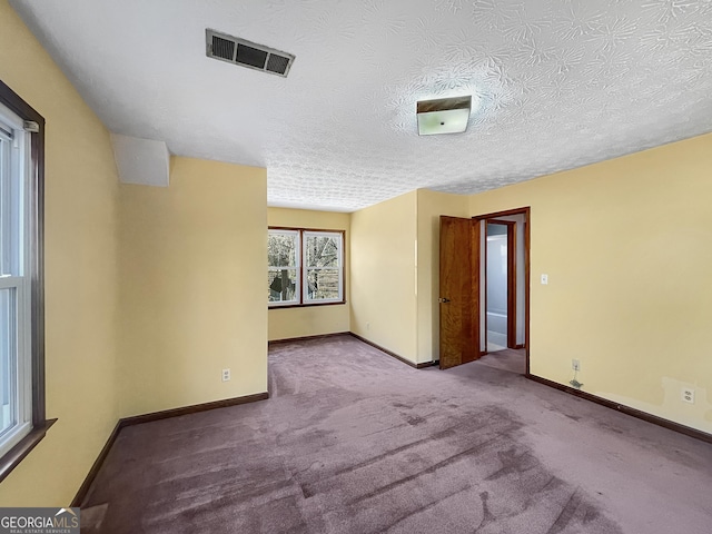 carpeted spare room with baseboards, visible vents, and a textured ceiling