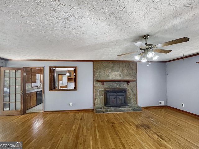 unfurnished living room featuring visible vents, hardwood / wood-style floors, a stone fireplace, crown molding, and baseboards