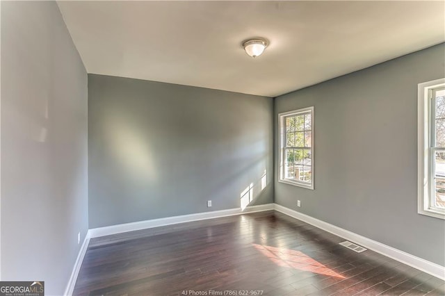 unfurnished room with visible vents, dark wood-type flooring, and baseboards