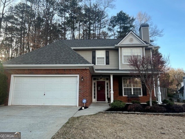 traditional home featuring brick siding, roof with shingles, a chimney, a garage, and driveway