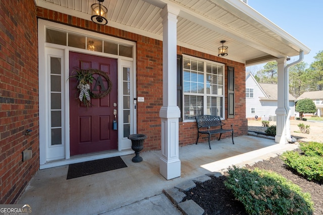 entrance to property featuring a porch and brick siding