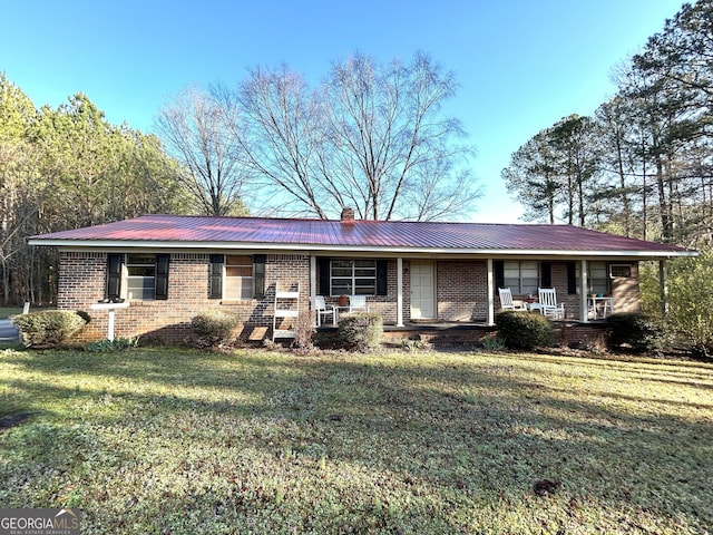 ranch-style home with a front yard, covered porch, a chimney, brick siding, and metal roof