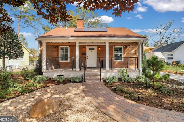 bungalow-style home with solar panels, covered porch, and a chimney