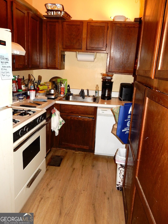 kitchen with white appliances, ventilation hood, a sink, light countertops, and light wood-style floors