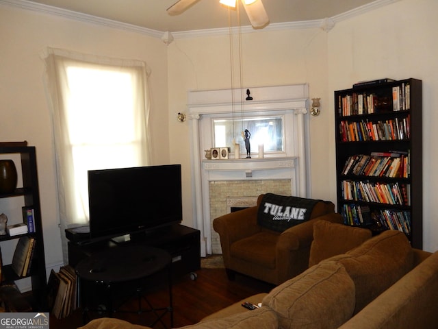 living area featuring wood finished floors, a fireplace, ornamental molding, and a ceiling fan