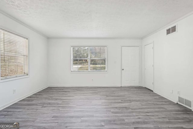 empty room with visible vents, a textured ceiling, wood finished floors, and ornamental molding