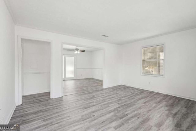 unfurnished room with visible vents, ornamental molding, wood finished floors, baseboards, and ceiling fan