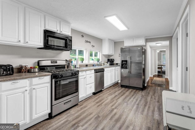 kitchen featuring light wood-style flooring, stainless steel appliances, white cabinets, a textured ceiling, and a sink