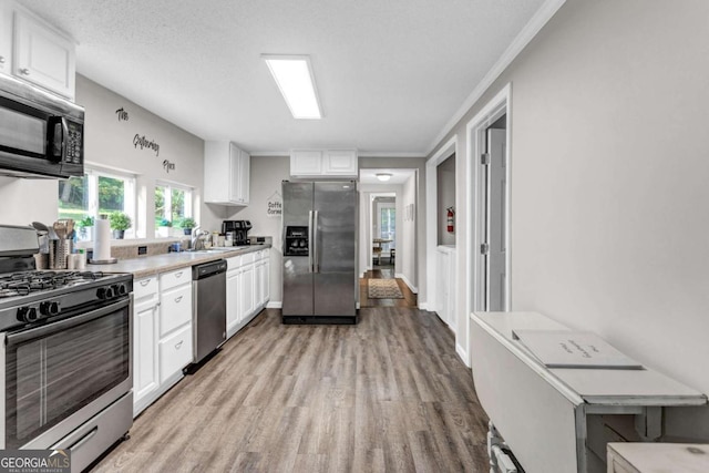 kitchen with light wood-type flooring, light countertops, appliances with stainless steel finishes, white cabinetry, and a sink