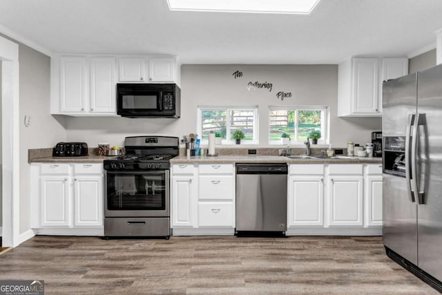 kitchen with light wood-style flooring, white cabinets, stainless steel appliances, and a sink