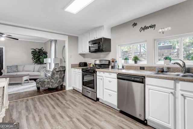 kitchen featuring light wood finished floors, a sink, ceiling fan, stainless steel appliances, and white cabinets