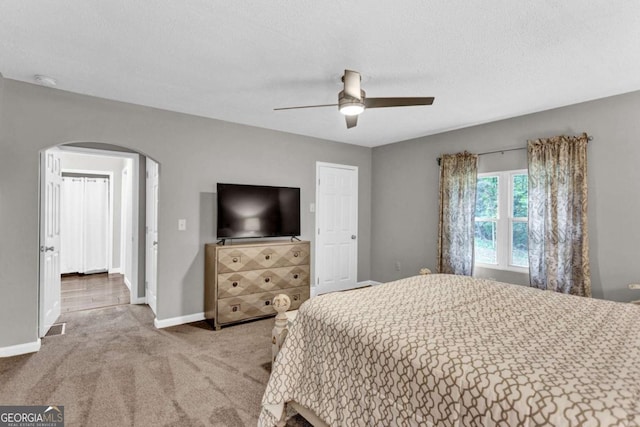 carpeted bedroom featuring a ceiling fan, visible vents, baseboards, arched walkways, and a textured ceiling