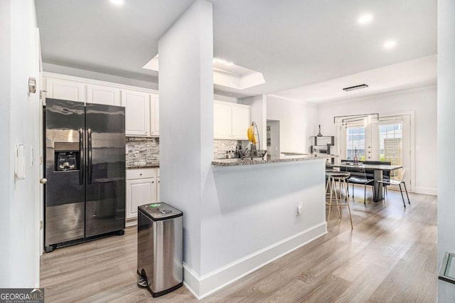 kitchen with a tray ceiling, decorative backsplash, light wood-style floors, white cabinetry, and black fridge