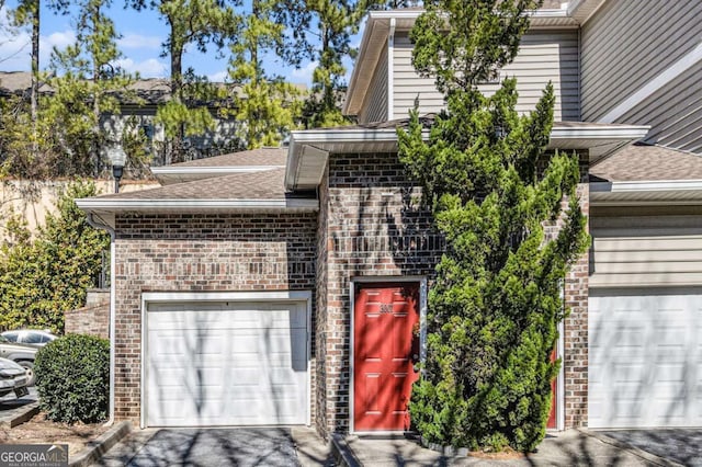 view of front facade with driveway, brick siding, an attached garage, and a shingled roof