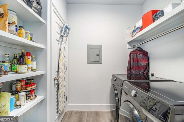 clothes washing area with baseboards, electric panel, laundry area, wood finished floors, and washer and dryer