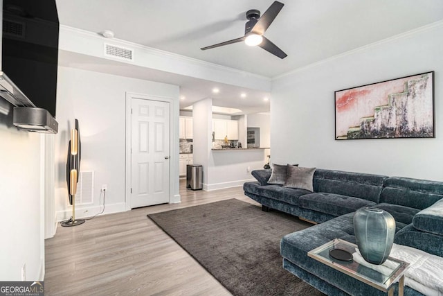 living area with crown molding, baseboards, visible vents, and light wood-type flooring