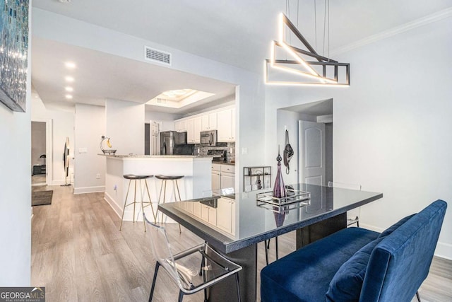 dining space featuring visible vents, a raised ceiling, ornamental molding, light wood-style floors, and baseboards