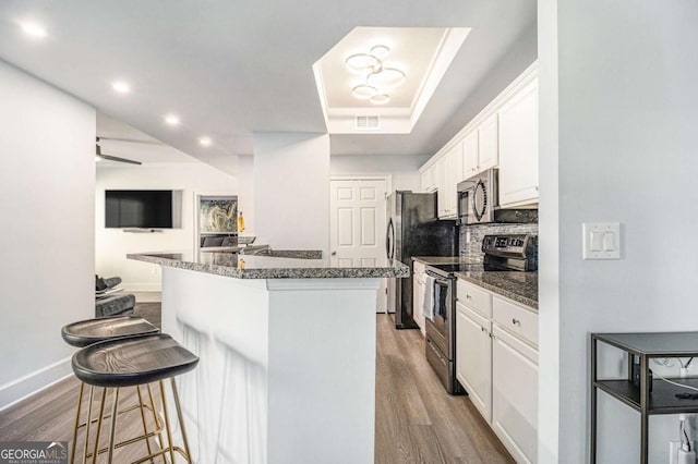 kitchen featuring wood finished floors, a breakfast bar area, white cabinets, and appliances with stainless steel finishes