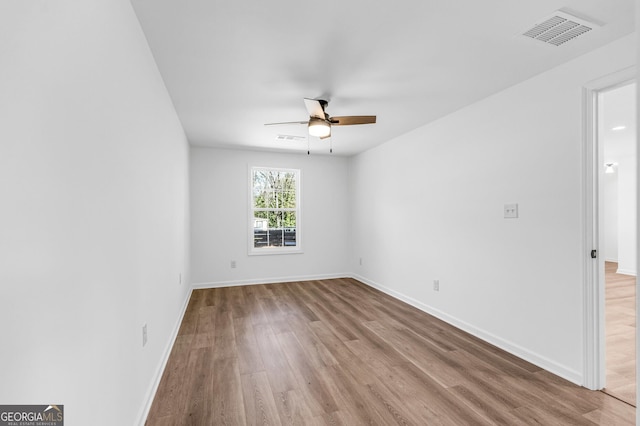 empty room with wood finished floors, a ceiling fan, visible vents, and baseboards