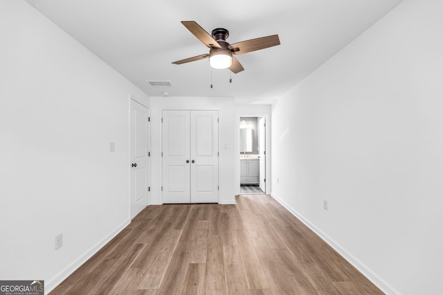 unfurnished bedroom with wood finished floors, visible vents, a closet, and baseboards