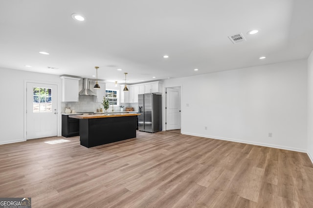 kitchen with light wood finished floors, a center island, stainless steel fridge, wall chimney exhaust hood, and light countertops