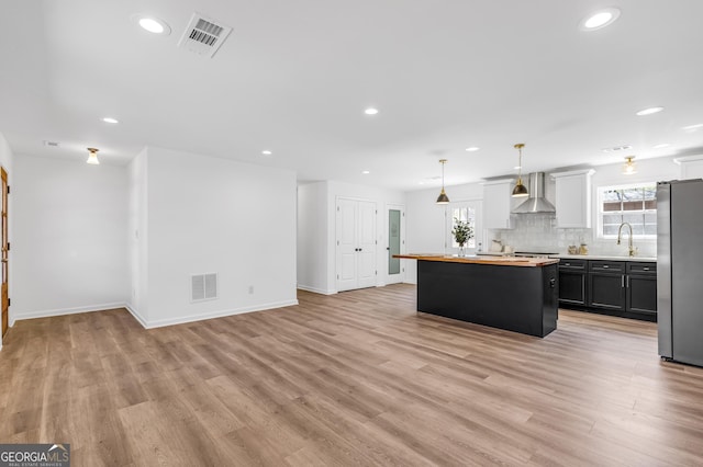 kitchen featuring visible vents, light wood finished floors, a sink, freestanding refrigerator, and wall chimney range hood