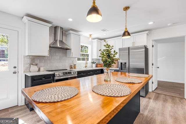 kitchen featuring visible vents, backsplash, butcher block countertops, stainless steel appliances, and wall chimney exhaust hood