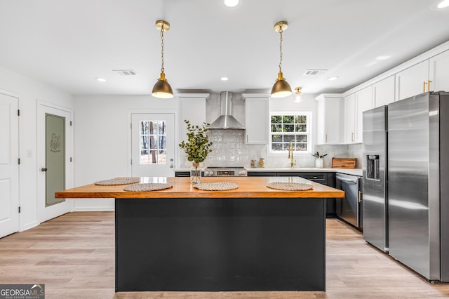 kitchen with visible vents, butcher block countertops, appliances with stainless steel finishes, wall chimney range hood, and a center island