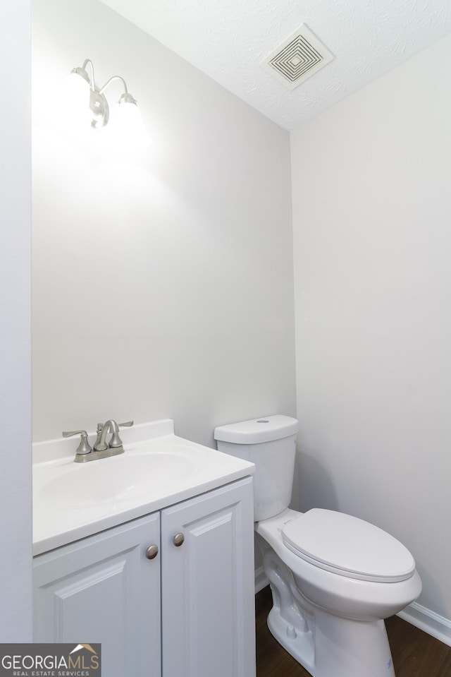 bathroom with vanity, wood finished floors, visible vents, a textured ceiling, and toilet