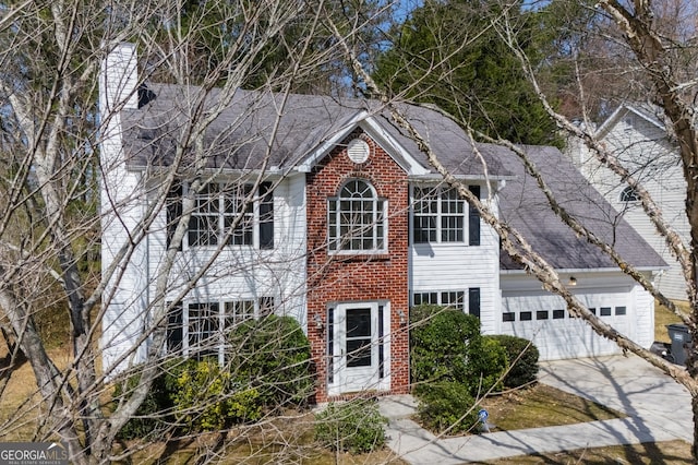 colonial house with brick siding, an attached garage, roof with shingles, a chimney, and driveway